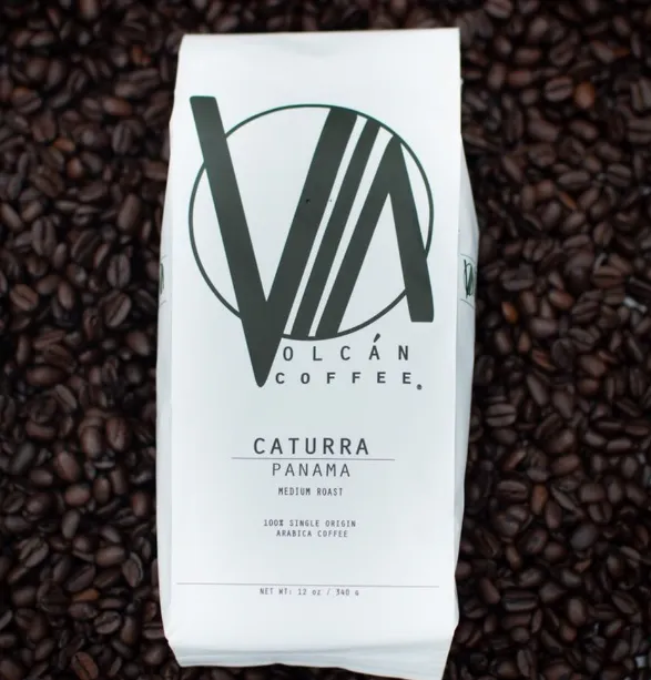White Vía Volcán Caturra Panama coffee bag lying on roasted coffee beans