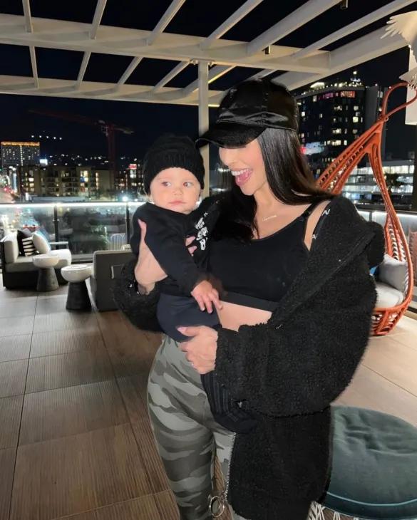Holding a baby on the rooftop deck at night with the city lights behind